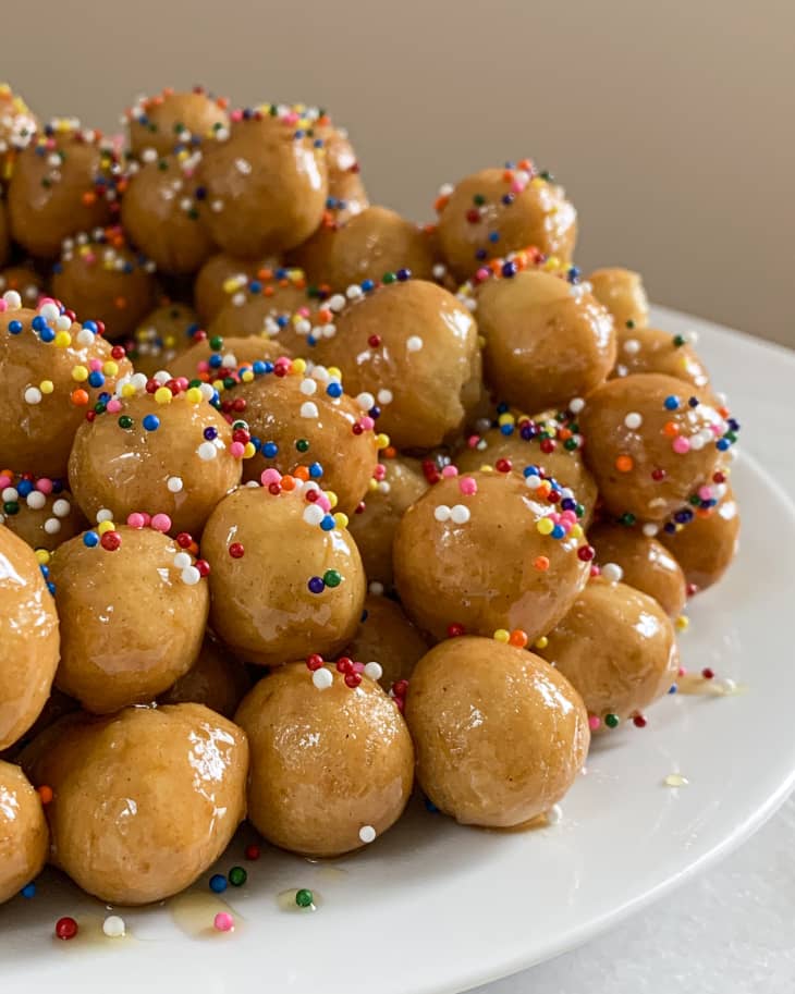 Struffoli, (Italian Honey Balls - very small crunchy dough balls mixed with honey and decorated with rainbow sprinkles) on a white plate.
