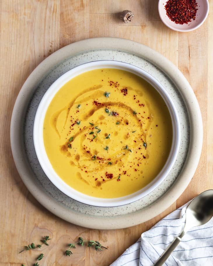 A pureed acorn squash soup in a white ceramic bowl with red spices sprinkled on top