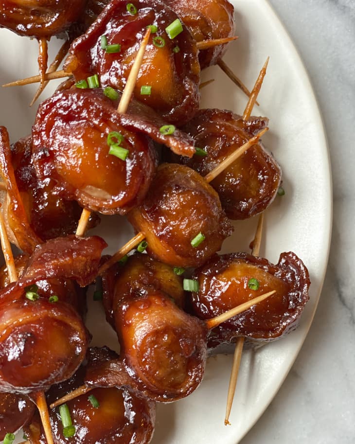 Bacon wrapped water chestnuts on a white plate, with toothpicks going through them.