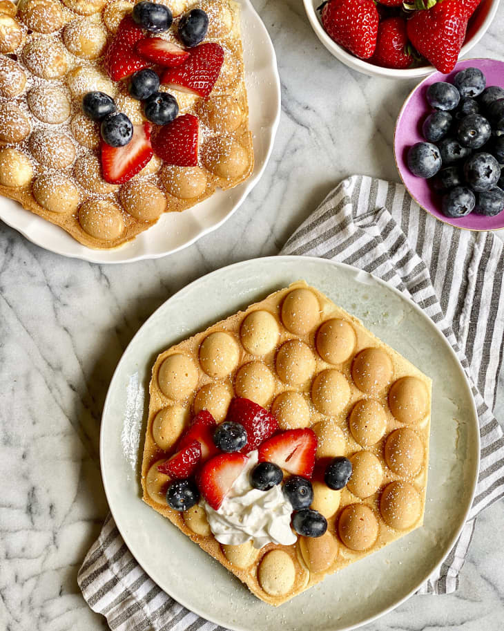 Bubble waffles on a plate with powdered sugar and fruit and whipped cream topping
