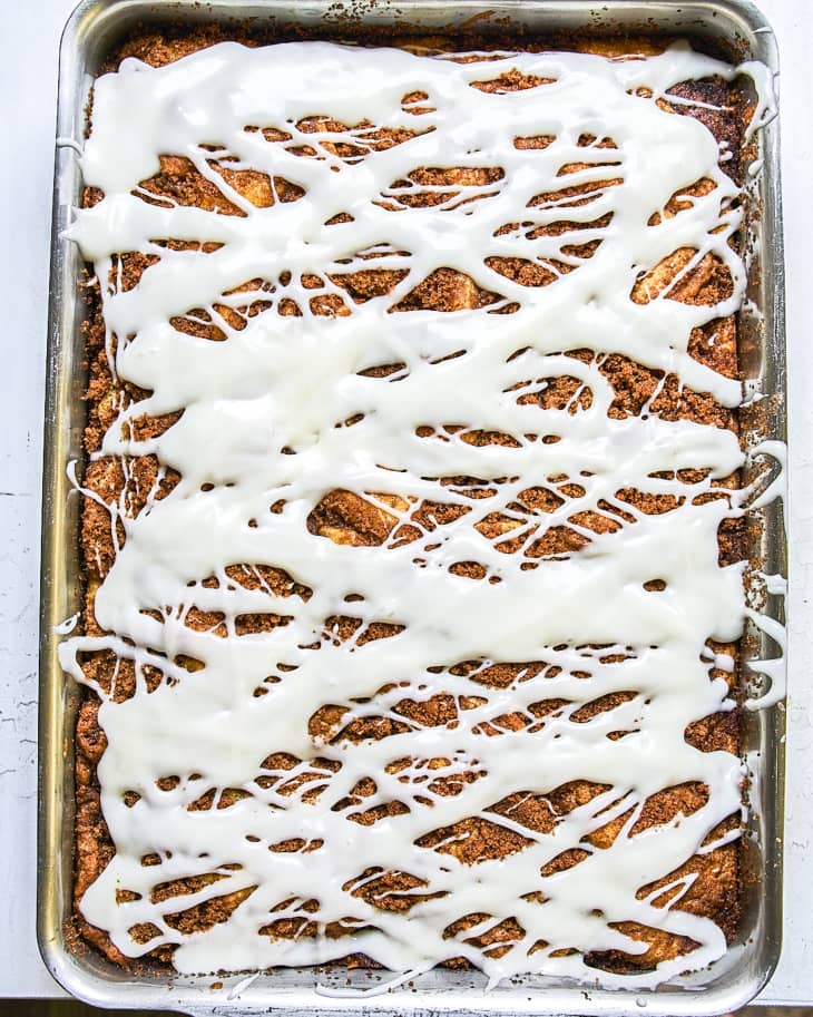 a whole cinnamon roll cake in a baking pan drizzled with white icing.