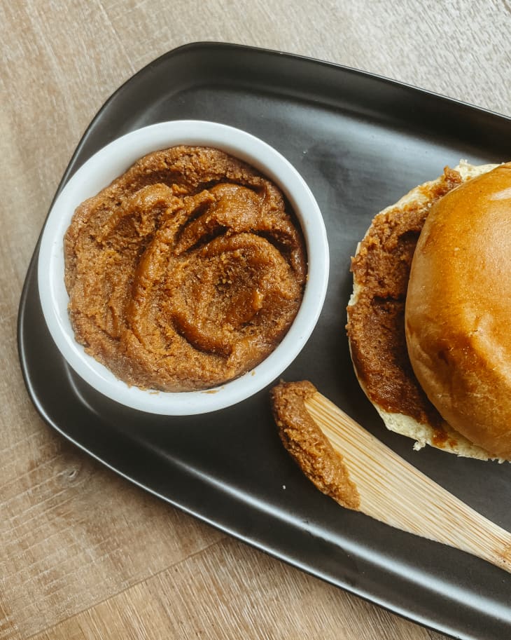 cookie butter in a bowl, on a black ceramic tray, with a roll and a wooden knife