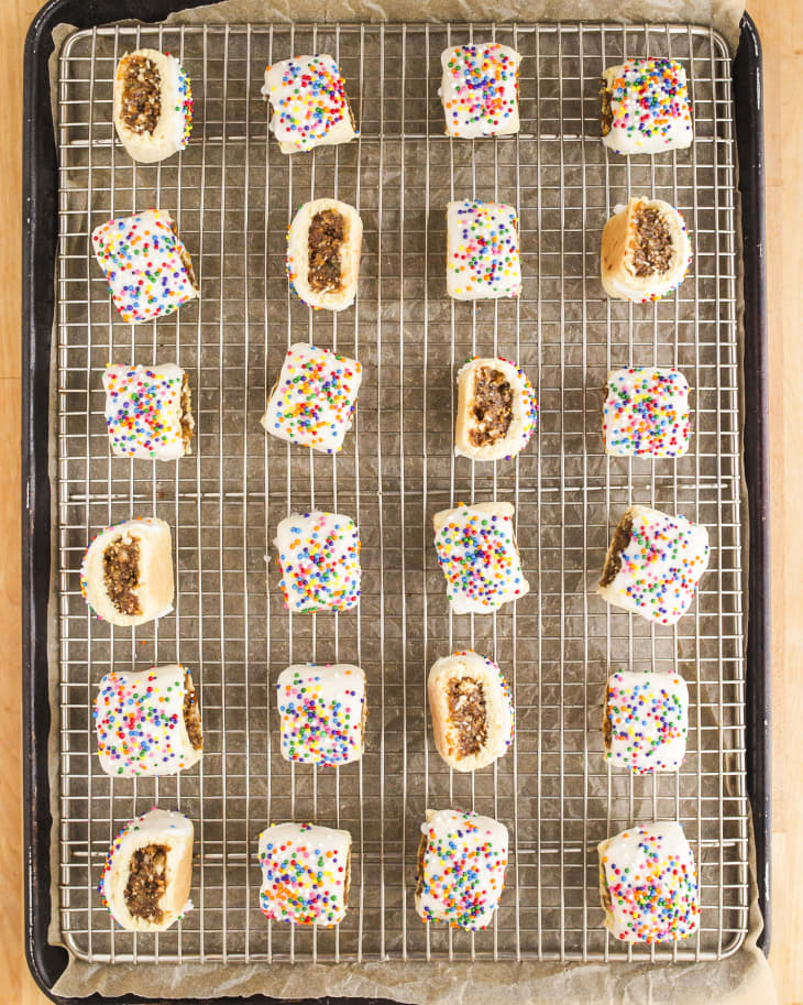 Cucidati (Italian fig cookies, where the outer cookie is pastry dough, covered with icing and topped with rainbow sprinkles) on a cooling rack
