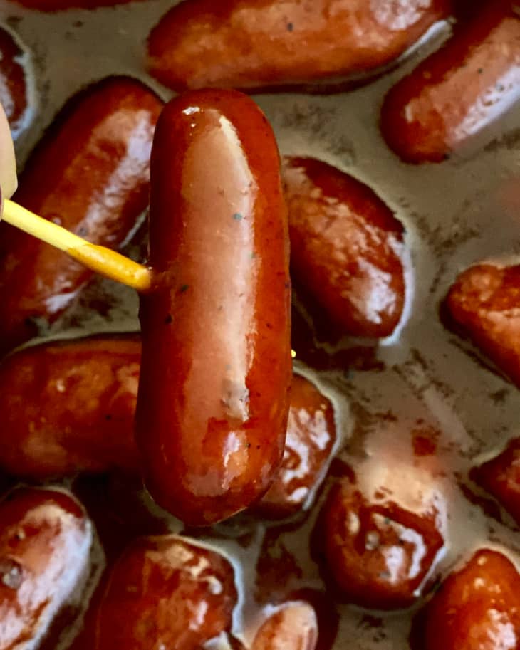 Little smokies (miniature smoked sausage links slowly cooked in sweet BBQ sauce), with one being lifted up by a toothpick