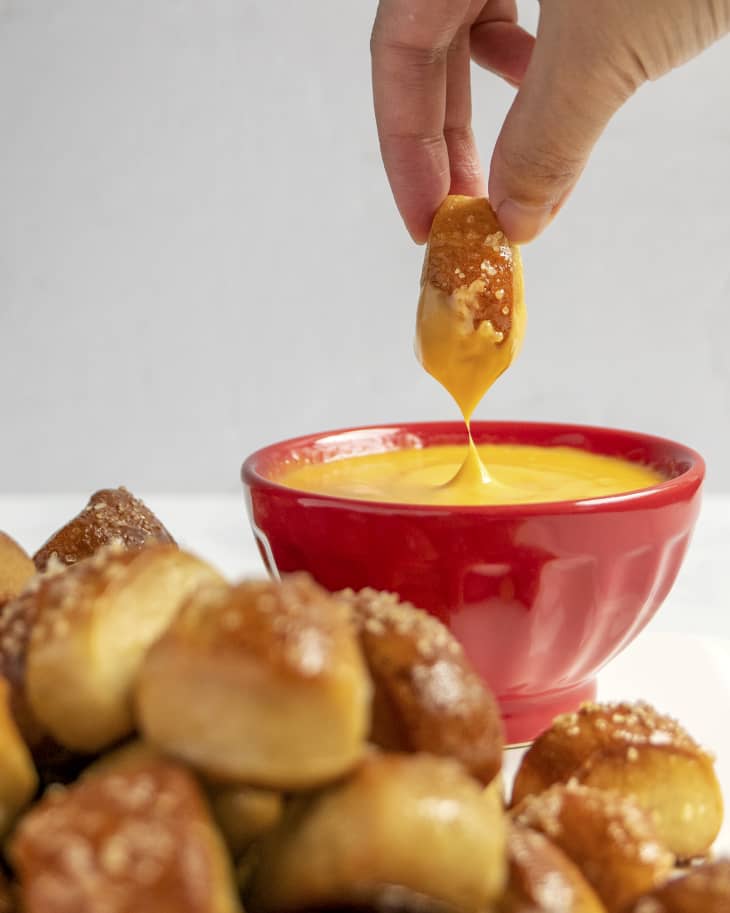 Pretzel bites with a honey mustard dipping sauce in a small red bowl with a hand dipping a pretzel bite into the sauce.