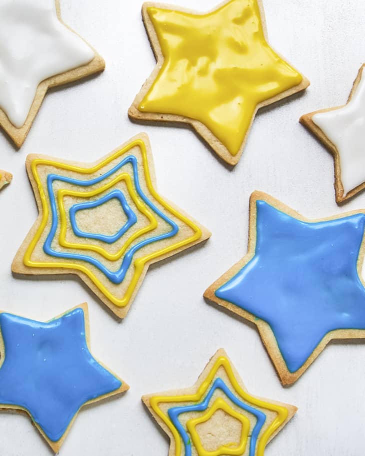 sugar cookies in the shape of stars with blue, yellow and white icing decorating the cookies in various designs, with some of the cookies iced in a single, solid color