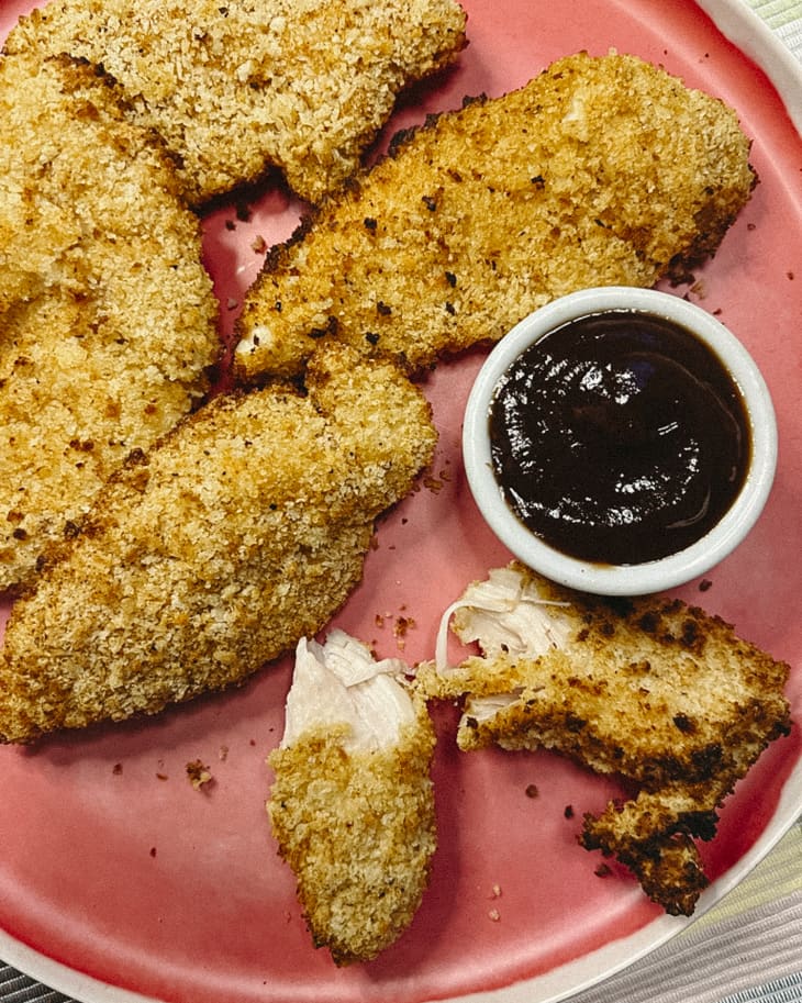 Chicken tenders on a pink plate with a dipping sauce on the side.