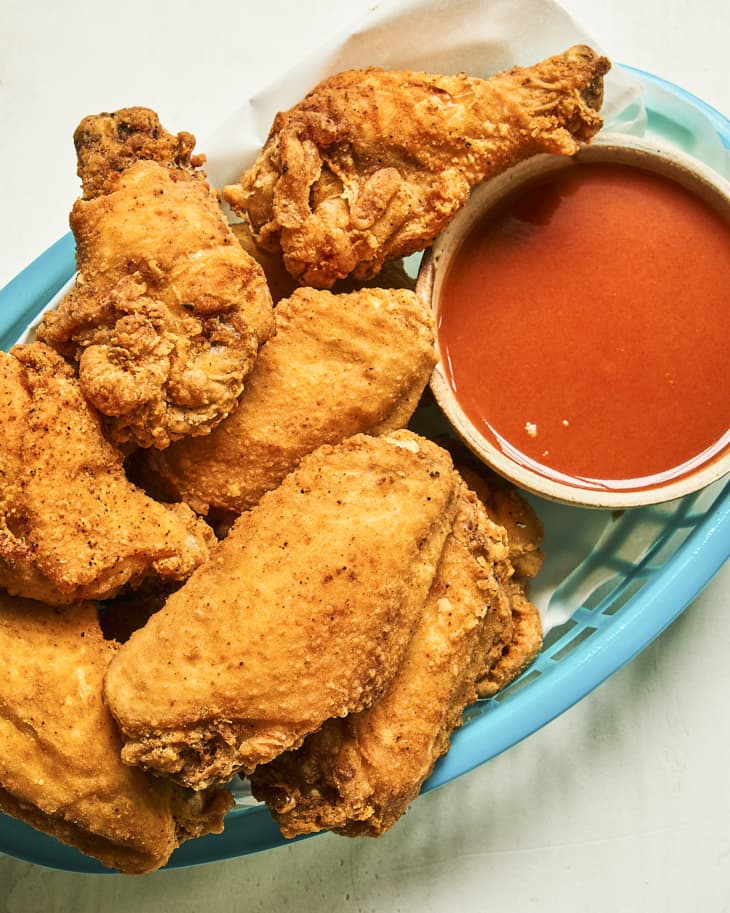 fried chicken wings in a turquoise basket, with buffalo sauce in a white ramekin on the side.