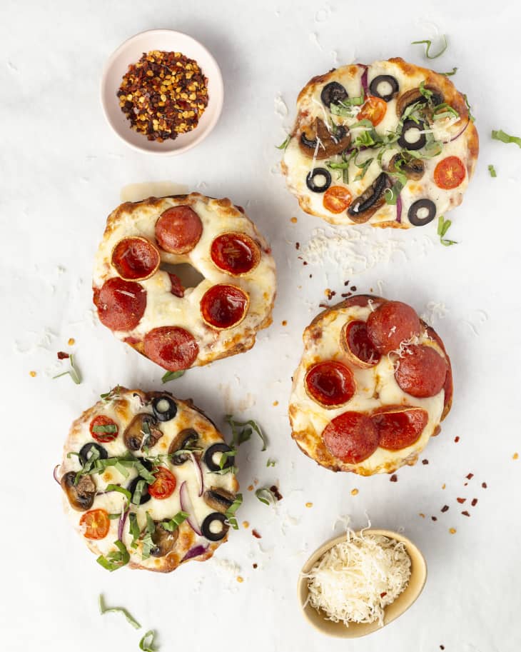 open faced pizza bagels with various toppings, seen from above, with a small ramekin of dried chili flakes and grated cheese on the side