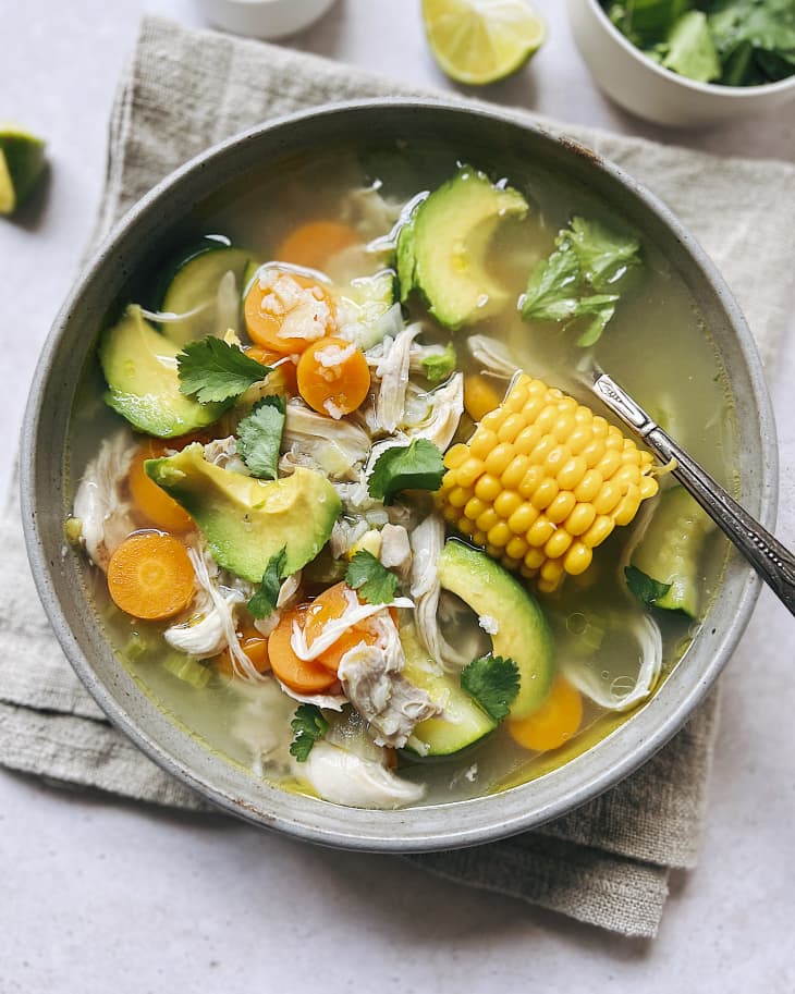 Caldo De Pollo (a common Latin American soup that consists of chicken and vegetables) garnished with avocado slices, in a gray bowl
