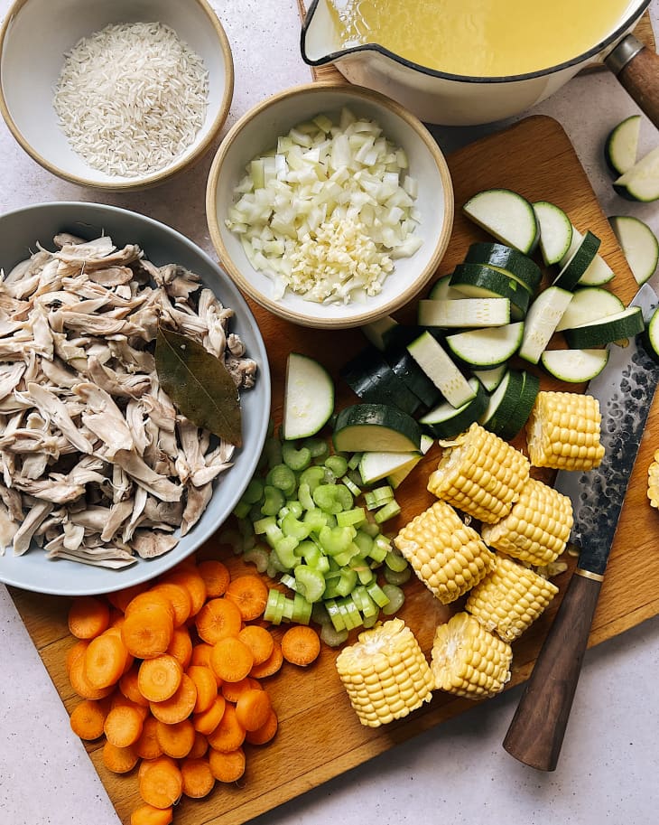 the ingredients for Caldo De Pollo (a common Latin American soup that consists of chicken and vegetables) on a cutting board, consisting of corn, carrots, and other ingredients