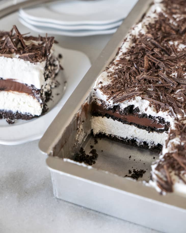 Chocolate lasagna (chocolate cream pie with alternating layers of chocolate and cream) in a tin with a piece cut out on a plate besides it