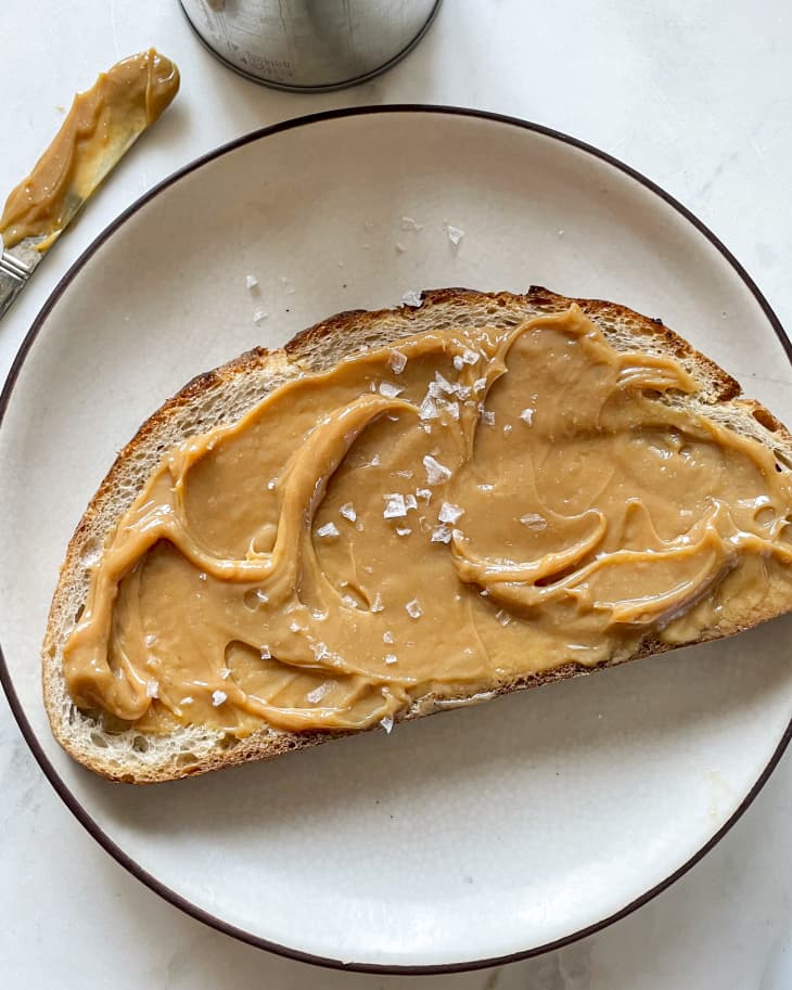 Dulce de leche (also known as caramelized milk or milk jam in English, is a confection from Latin America prepared by slowly heating sugar and milk over a period of several hours) spread on a piece of bread with some salt sprinkled on top