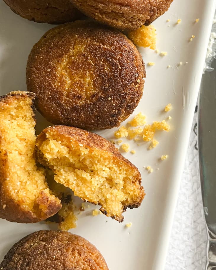 five individual round pieces of hot water cornbread on a rectangular white plater with one piece broken open in half and crumbs on the plate