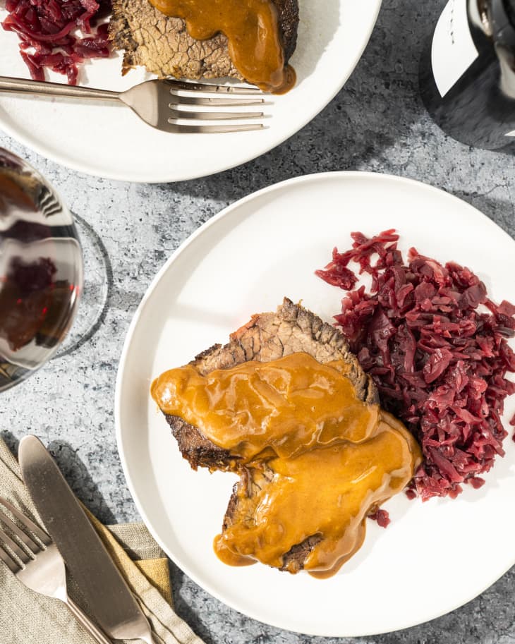 two slices of sauerbraten - roasted beef (Sauerbraten is a traditional German roast of heavily marinated meat. It is regarded as a national dish of Germany, and is frequently served in German-style restaurants internationally. It can be prepared from a variety of meats, most often from beef) on a white plate with a red cabbage side
