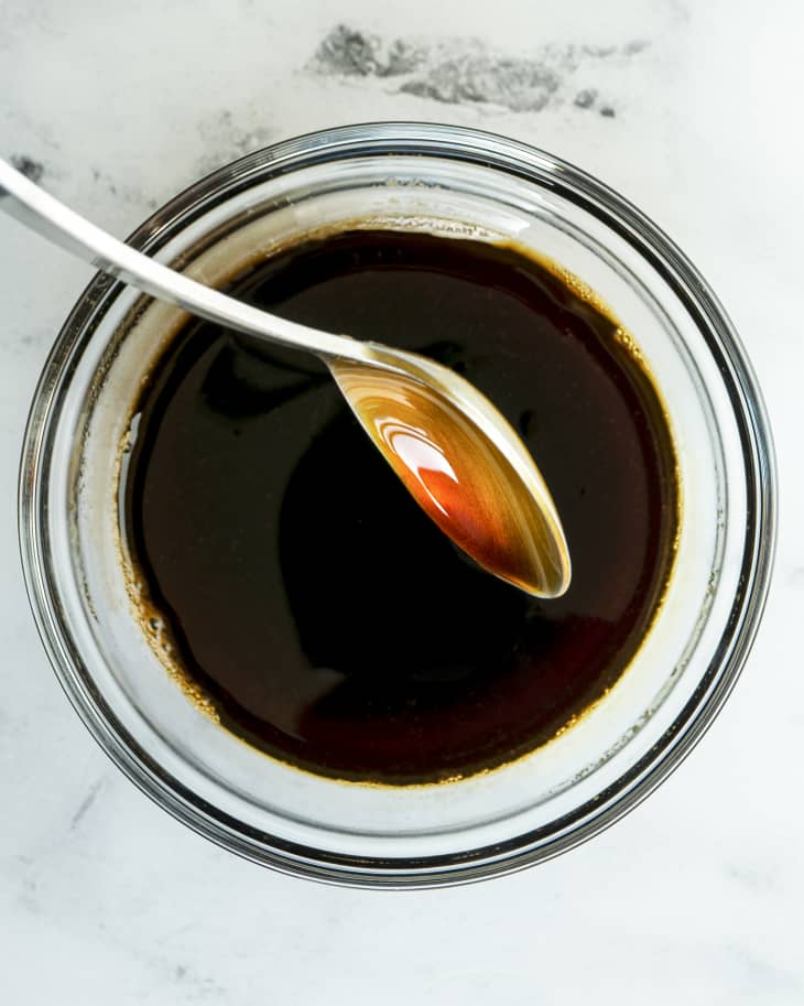 Teriyaki sauce in a small glass ramekin with a spoon picking up some of the sauce and letting it drip back into the ramekin.