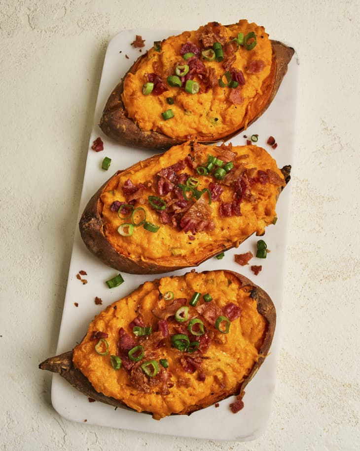 three twice baked sweet potatoes topped with bacon and scallions on a rectangular plate.