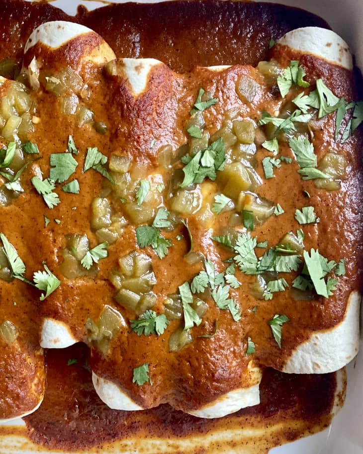 vegan enchiladas in a white baking pan with a green garnish sprinkled over the top.