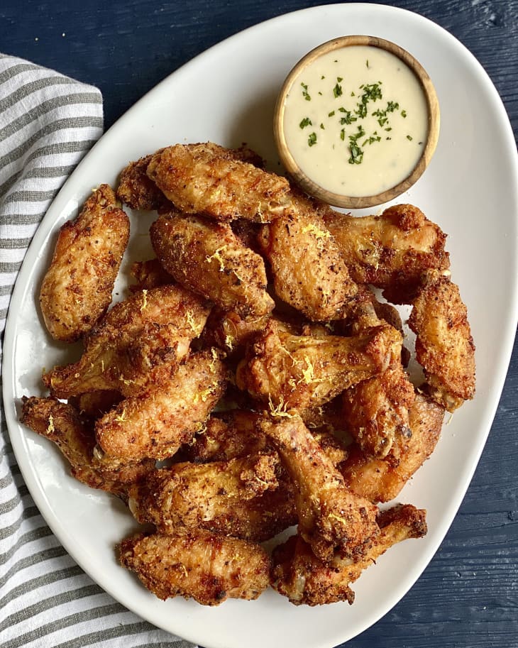 A pile of baked chicken wings on an oval plate with a blue cheese dipping sauce in a small ramekin on the plate next to them