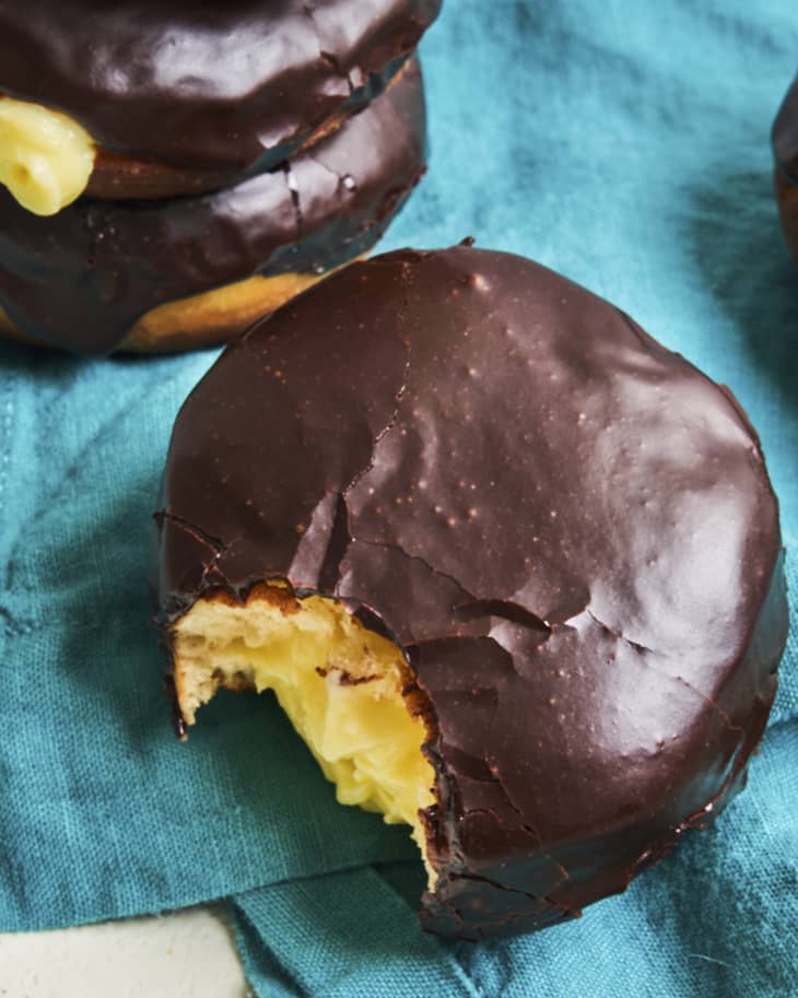 a boston cream donut with chocolate icing, with a bite taken out on a green cloth napkin