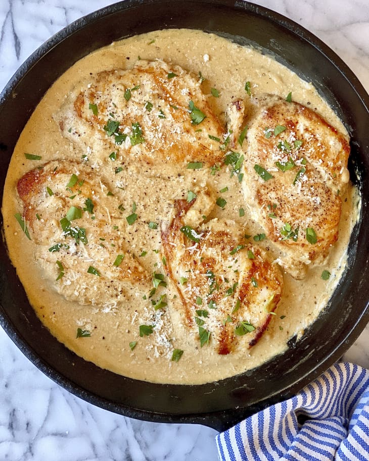 chicken breasts in a creamy brown sauce in a cast iron skillet.