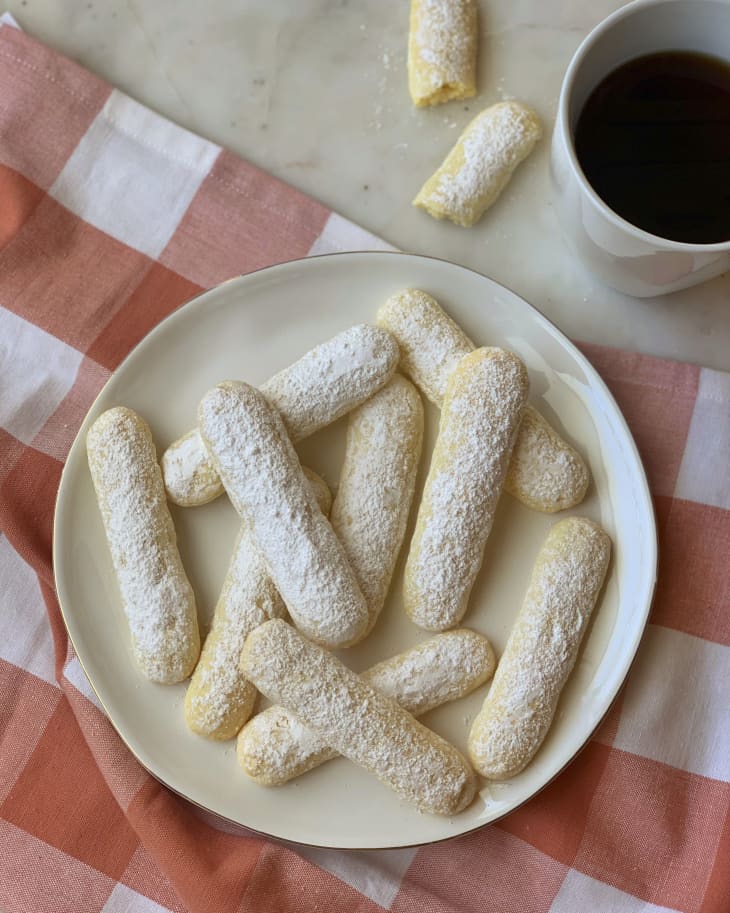 ladyfingers on a plate with a cup of coffee behind it