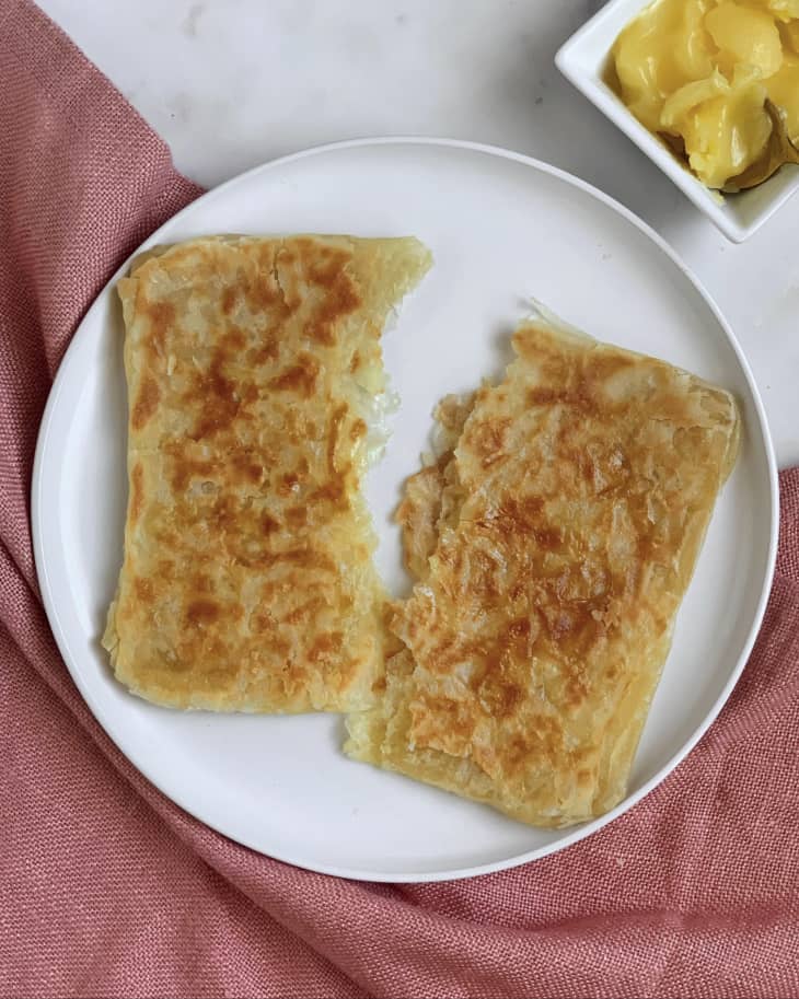 Paratha (a flatbread native to the Indian subcontinent) ripped in half on a white plate.
