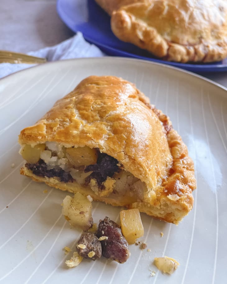 a pasty (A pastry case filled with beef, potato, and onion) on a plate cut in half