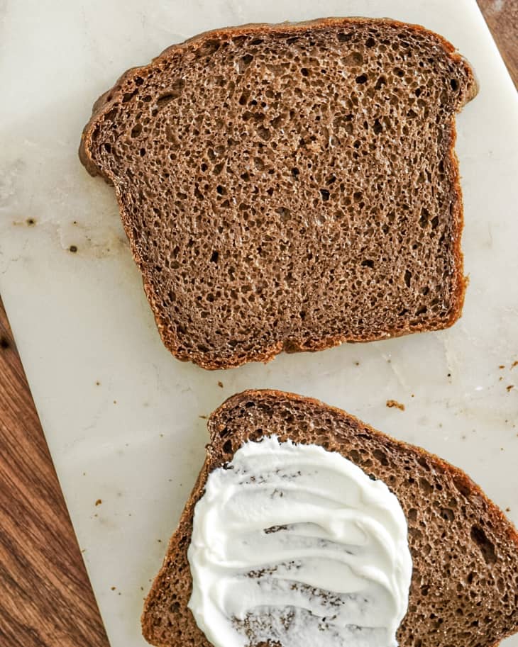 two slices pumpernickel bread with cream cheese spread on one slice.
