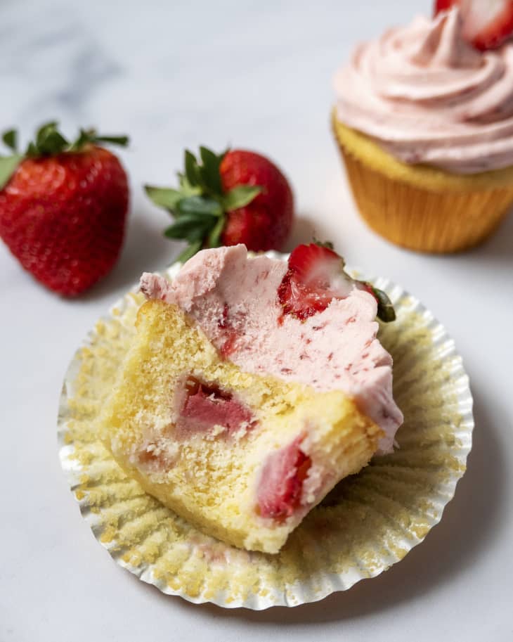 a yellow cupcake with strawberries baked into it, with a bite taken out of it, lying on its side.
