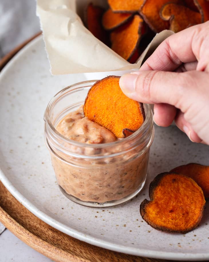 a sweet potato chip being dipped into an orange creamy dressing