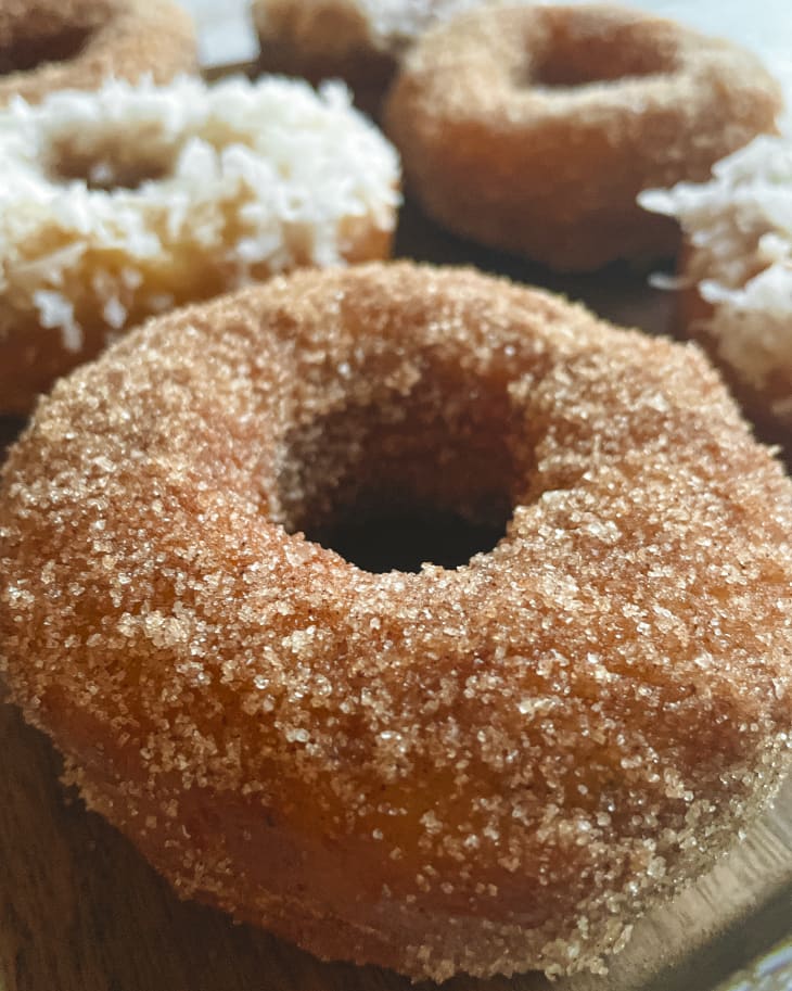 A closeup of a vegan donut with sugar coating on the outside with other flavored donuts in the background.