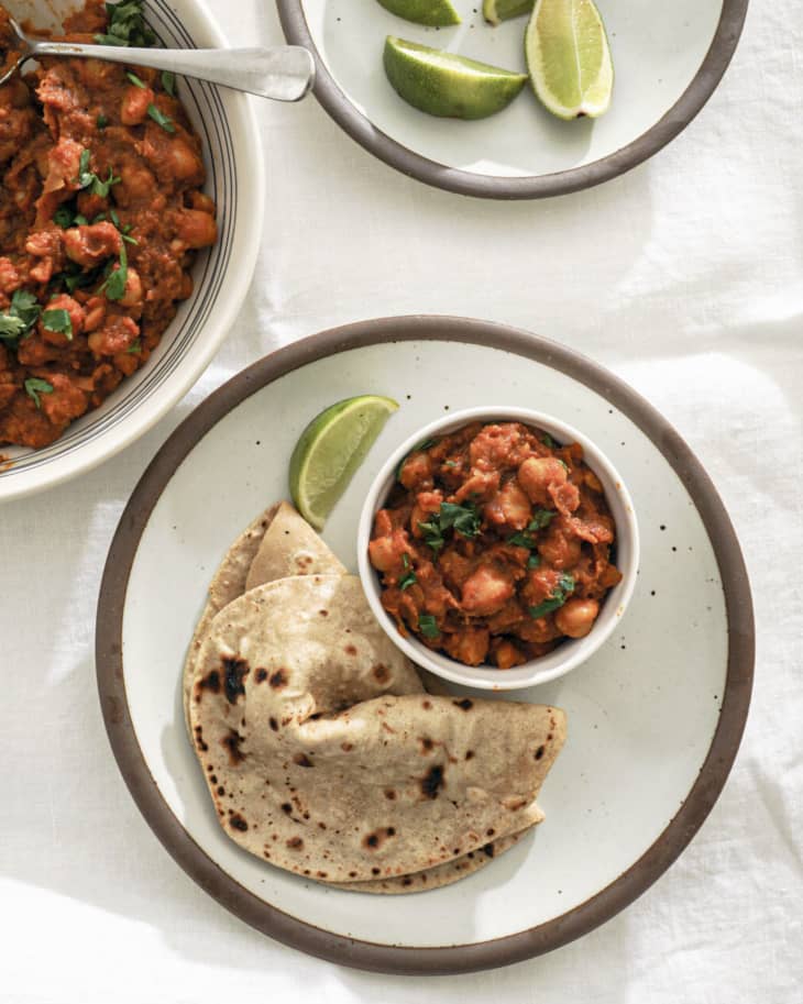 Indian chickpea curry (Chole) in a small white bowl with naan and lime wedges on the side