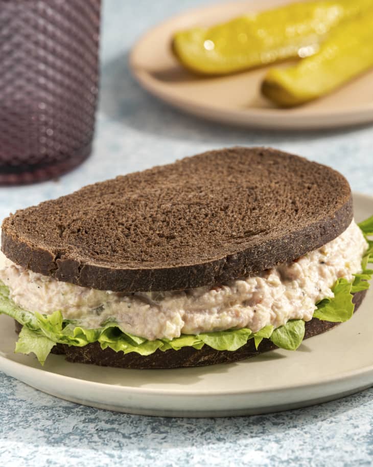 a ham salad sandwich on pumpernickel bread with pickle slices in the background
