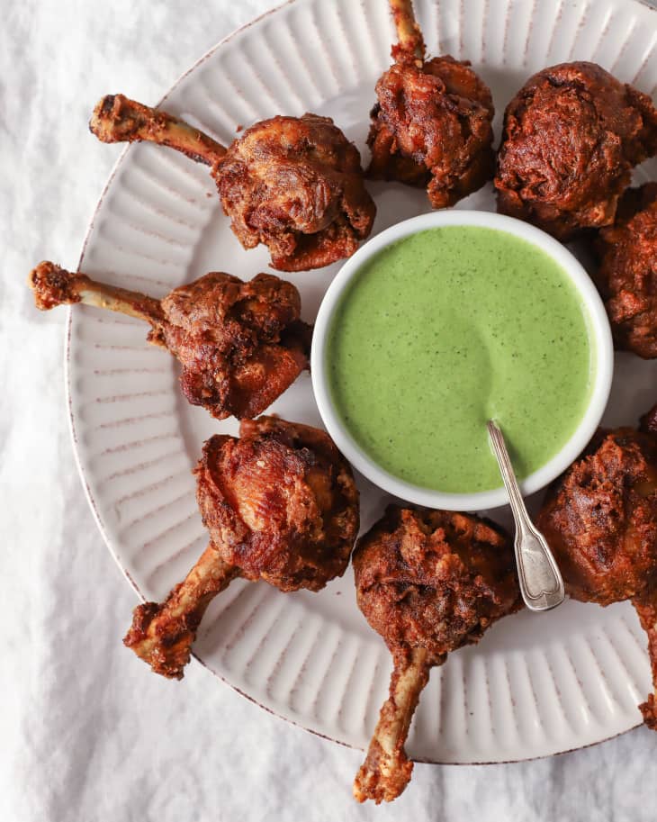 chicken lollipops (crispy batter-fried chicken wings made using chicken drumettes and wingettes) on a white plate with a ramekin of pale green sauce