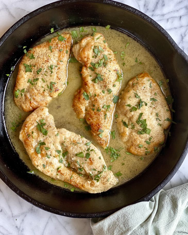 four pieces of chicken scallopini with a green garnish in a black skillet