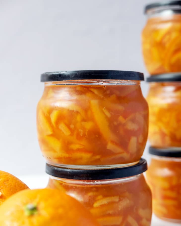 orange marmalade in a small rounded glass jar with a lid, stacked with other orange marmalade jars