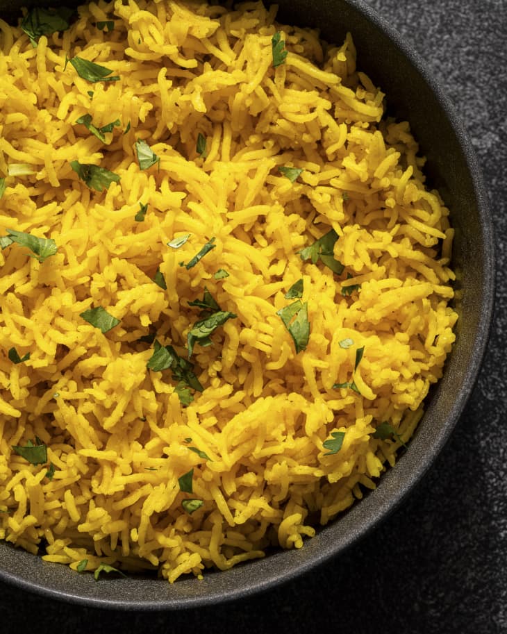 turmeric rice in a black skillet with a green garnish tossed in