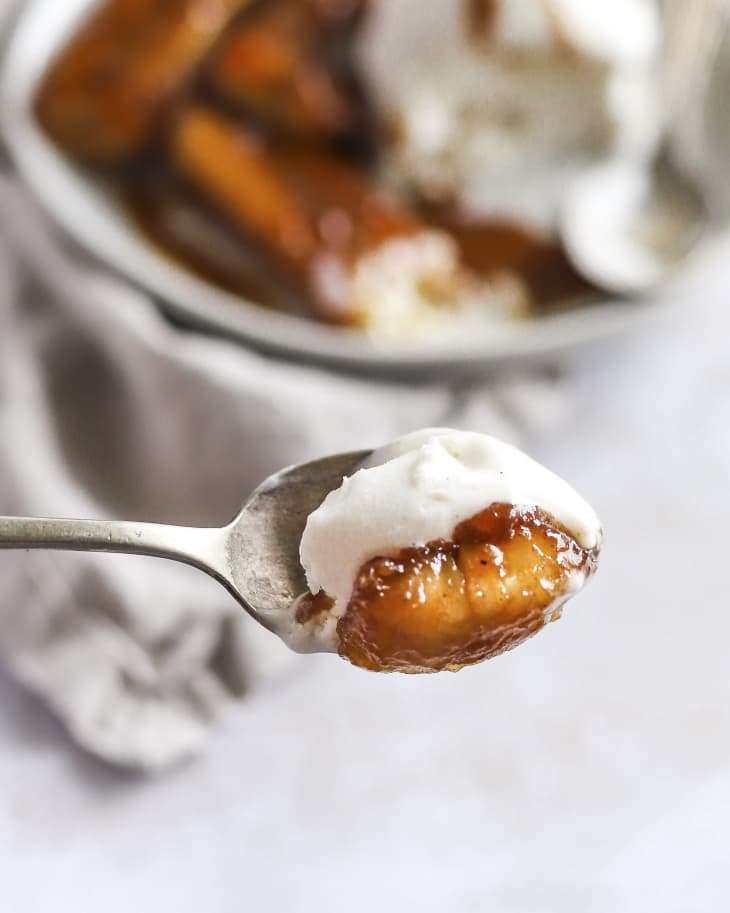 a spoon lifting up a spoonful of bananas foster (grilled bananas and vanilla ice cream)