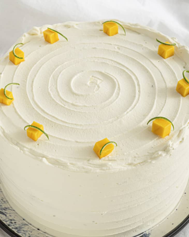 a round cake with white icing, with chunks of mango decorating the rim of the top of the cake.