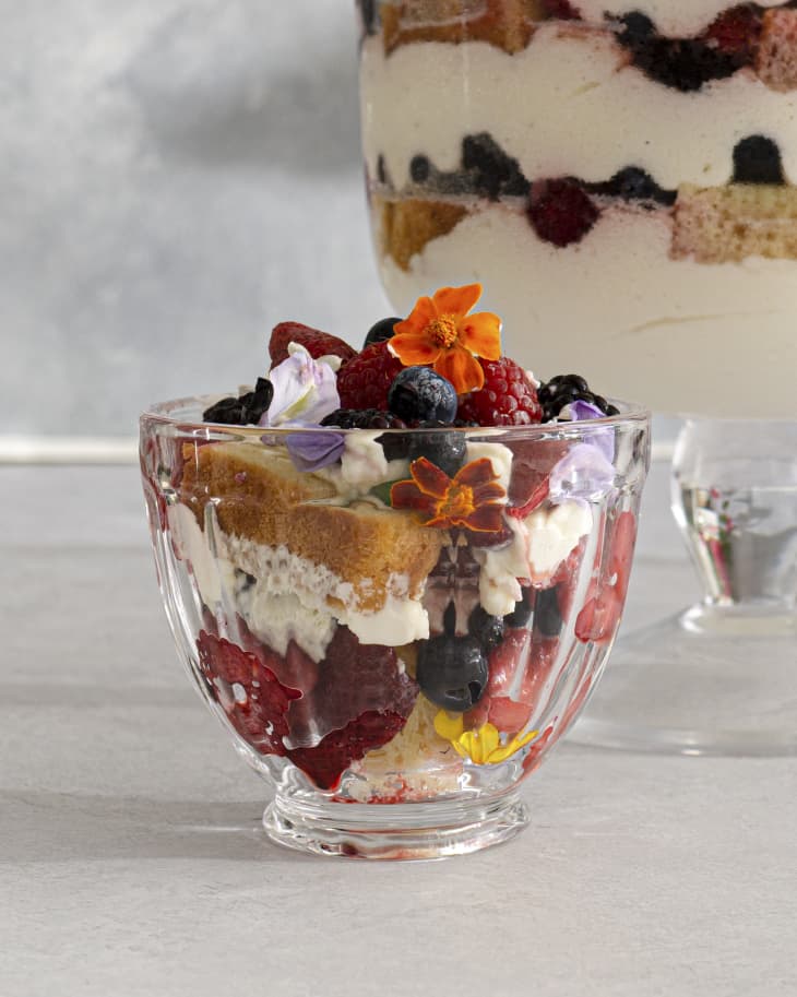 A small bowl with a portion of berry trifle with various berries and colorful edible flowers on top.