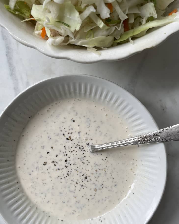 a bowl of white dressing with a spoon resting in the bowl, and a cabbage mix on the side