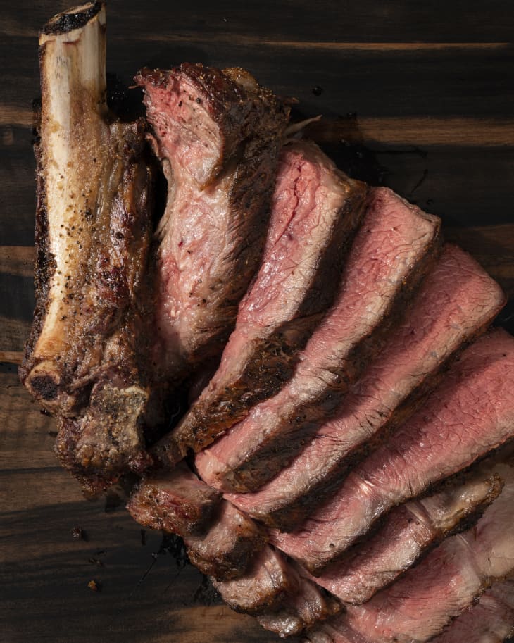 A grilled, cowboy steak (a thick bone-in ribeye cut between the ribs), cut into even slices.