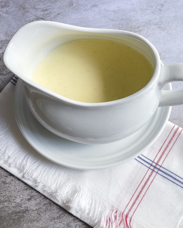 A photo of a white gravy boat with creme anglaise (also known as custard sauce or pouring custard), a light, sweetened pouring custard used as a dessert cream or sauce.
