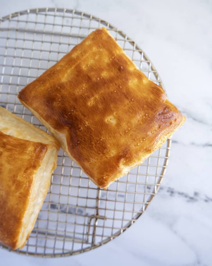 A photo of two square pastries on a round cooling rack, baked with an egg wash on top.