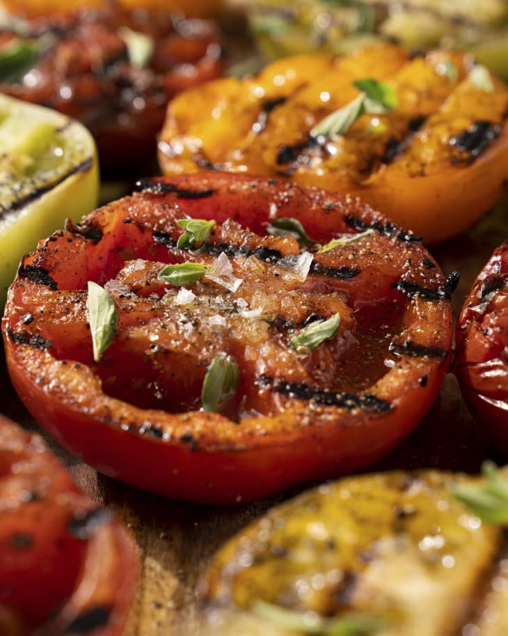 a closeup of slices of different colored grilled tomatoes, with a green garnish sprinkled on top