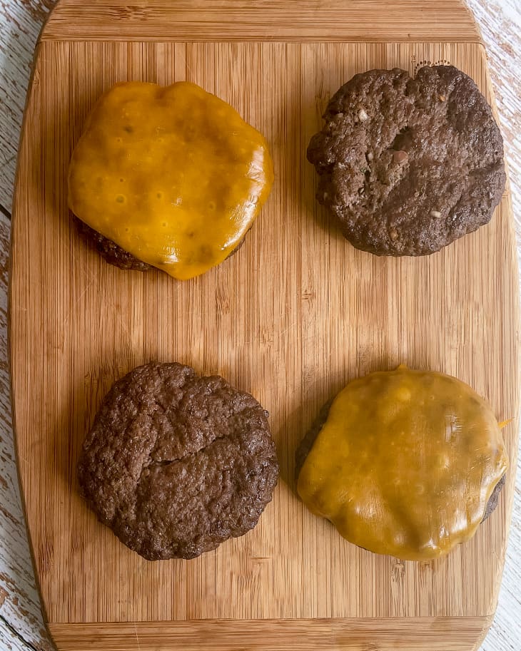 A photo of four burgers as seen from the top down. Two burgers (the top left and bottom right) have orange melted cheese on top.