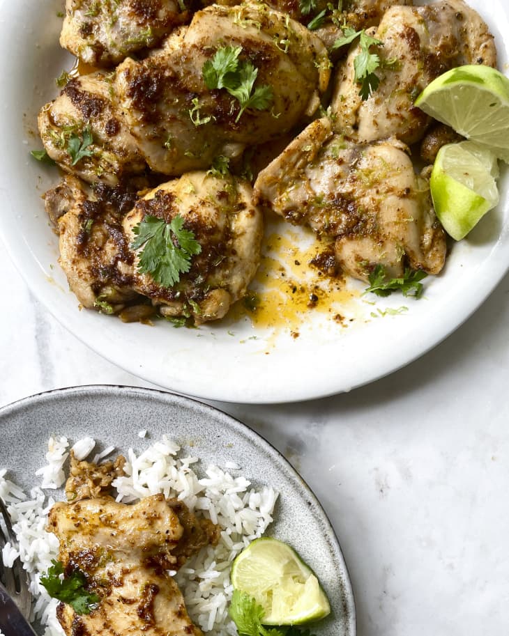 A photo of a plate of pan fried chicken thighs with a green garnish and limes on the side.