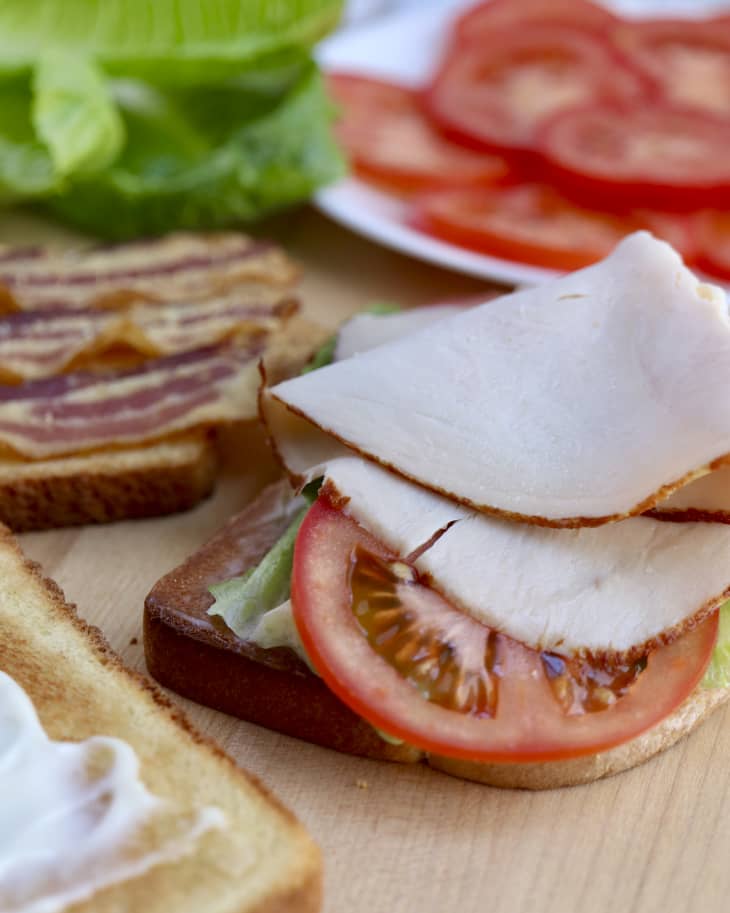 A photo of a disassembled club sandwich with toasted bread, lettuce, bacon, turkey and tomatoes.
