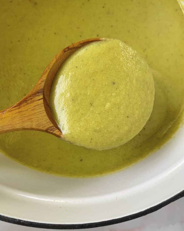 A photo of a round, wooden spoon lifting a spoonful of cream of broccoli soup.